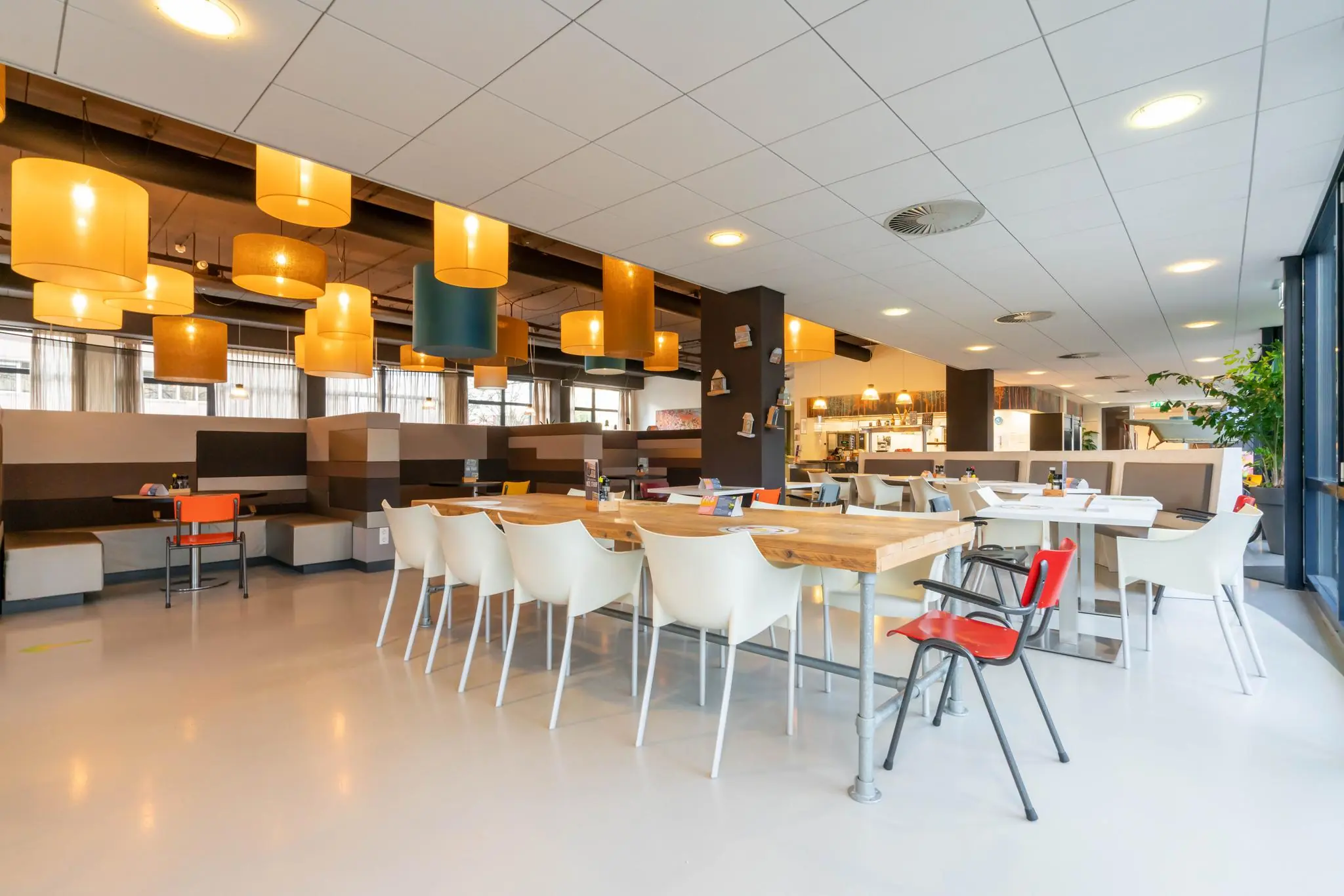 Moderne en kleurrijke eet- en ontmoetingsruimte aan de De Bruyn Kopsstraat met houten tafels, diverse stoelen en opvallende hanglampen.